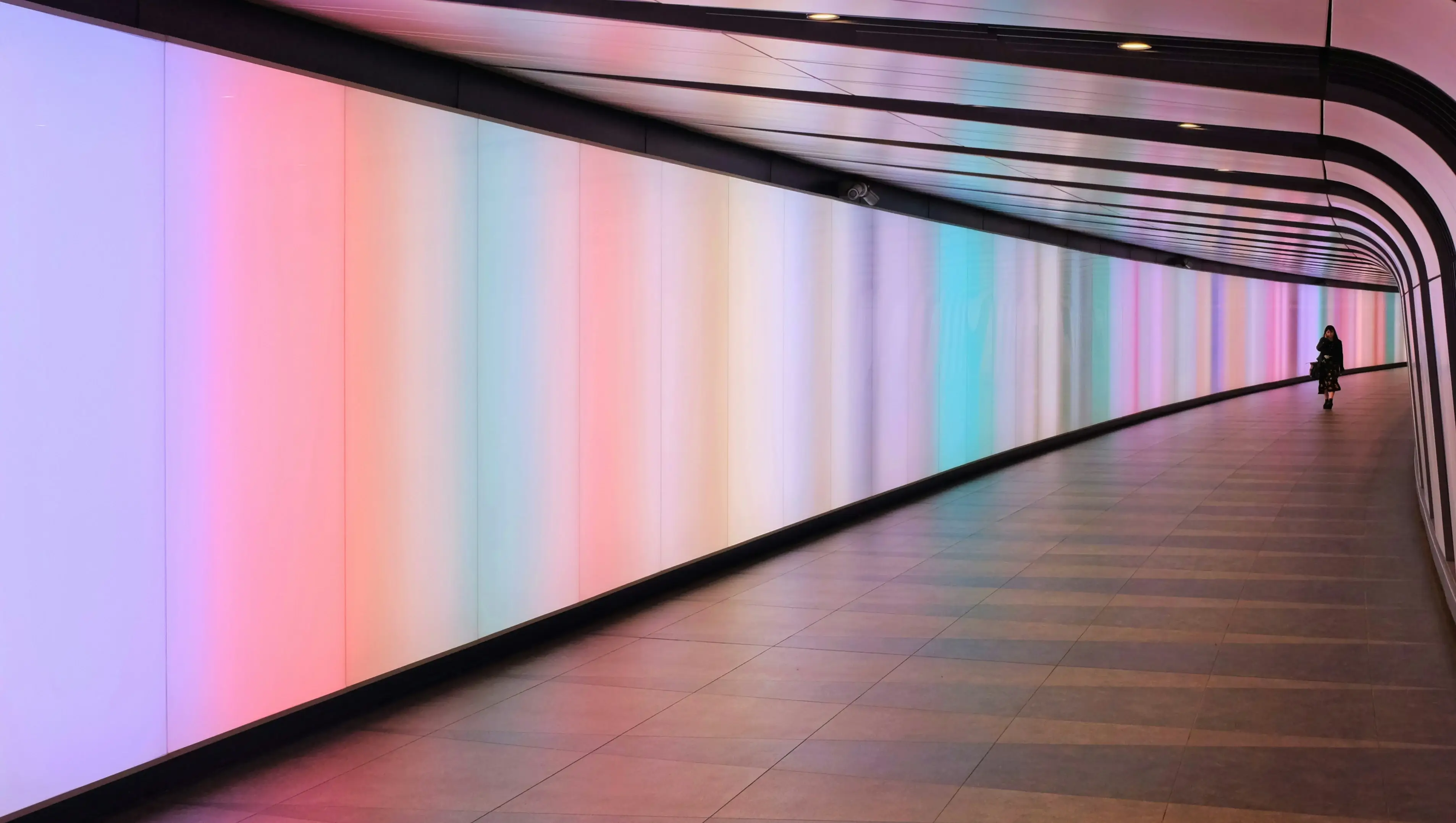 A lady walks along a long wall, captivated by the vibrant colors displayed on a stunning transparent LED screen.